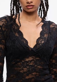 Zwarte kanten body met een diepe V-halslijn en bloemenpatronen, lange mouwen en een zachte, doorzichtige textuur. Gedetailleerde accenten rond de halslijn.