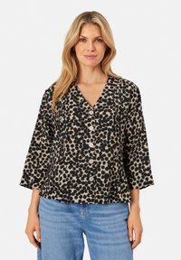 Blusa nera a pois con scollatura a V, maniche a tre quarti e bottoni frontali. Il tessuto ha una finitura testurizzata su uno sfondo chiaro.