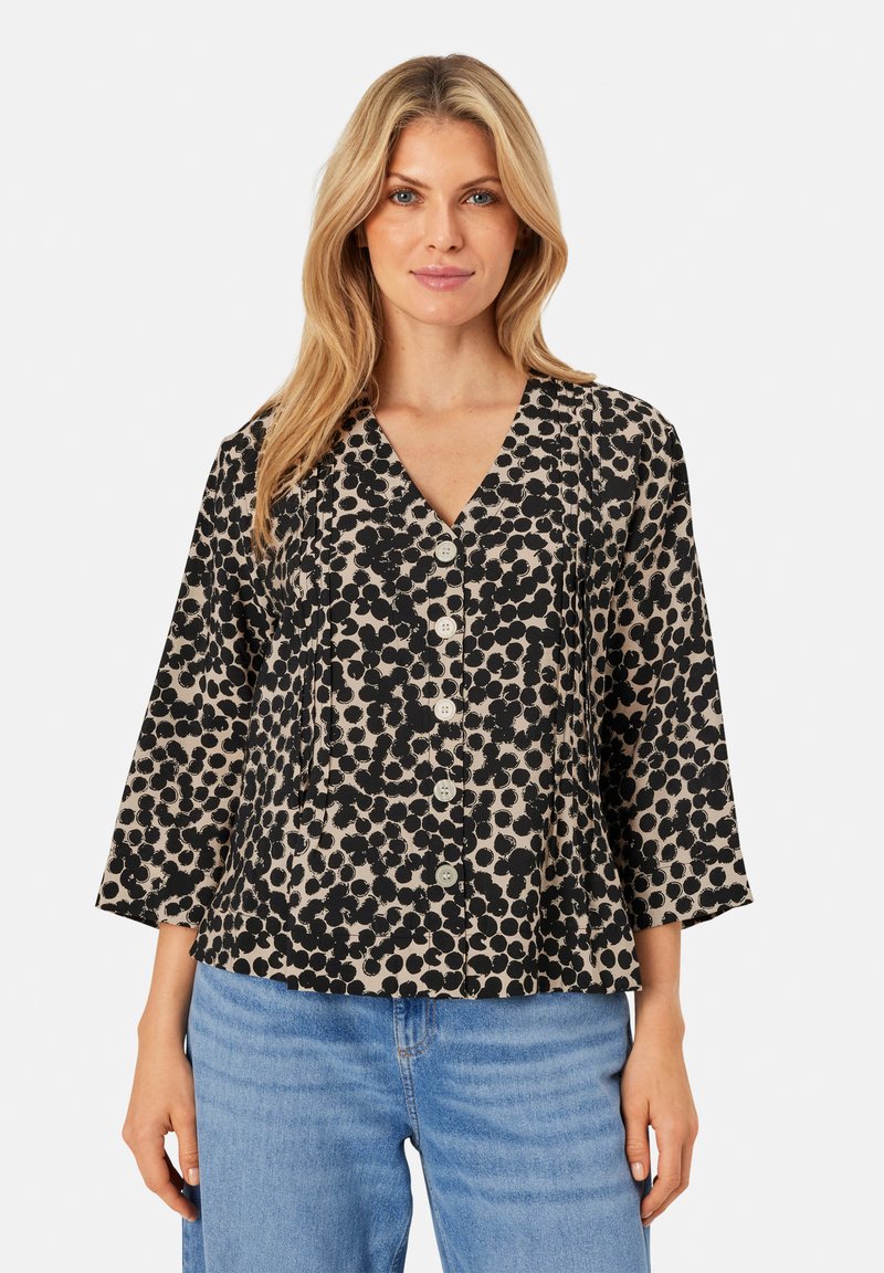 Blusa nera a pois con scollatura a V, maniche a tre quarti e bottoni frontali. Il tessuto ha una finitura testurizzata su uno sfondo chiaro.
