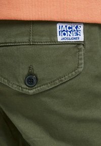 Pantaloni verde oliva con una tasca posteriore dotata di un bottone nero e un'etichetta bianca con testo blu "JACK & JONES". Tessuto morbido.