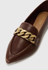 Kauboilasista nahkaa oleva ruskea loafer-kengät, jossa on terävä kärki ja kultaketju aksentti edessä. Sileä pinta, jossa on ommeltuja yksityiskohtia.