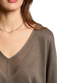 Maglione marrone a scollo a V con un motivo a maglia strutturato e un motivo geometrico sul collo, abbinato a una delicata collana con piccole perle.