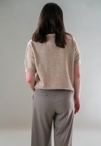 Beige gebreid T-shirt met korte mouwen en een relaxed fit, gecombineerd met lichtgrijze, geplooide broekspijpen met een wijde pasvorm en achterzakken.