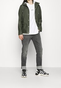 Green waterproof jacket with a hood, front pockets, paired with a white shirt, gray jeans, and black and white sneakers.