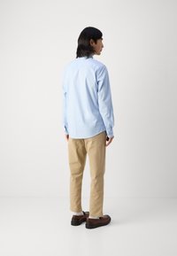 Chemise à manches longues bleu clair, pantalon beige, chaussures marron. Tissu doux, poignets boutonnés, coupe décontractée et design minimaliste.