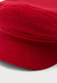 Um chapéu peludo vermelho brilhante com um detalhe de corda torcida ao longo da base da coroa, apresentado contra um fundo claro e simples.