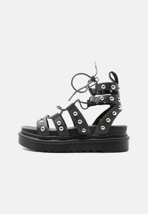 Black platform sandal with multiple studded straps and ankle lace-up closure on plain white background.