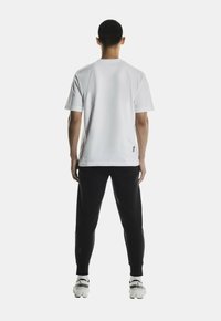 Witte katoenen t-shirt met ronde hals, gecombineerd met zwarte sweatpants. De broek heeft een aansluitende enkel en logo-detail bij de zoom.
