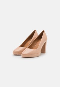 Escarpins à talons hauts en cuir verni couleur nude avec un bout carré, dotés d'un talon épais et d'une texture lisse, conçus pour une tenue formelle.