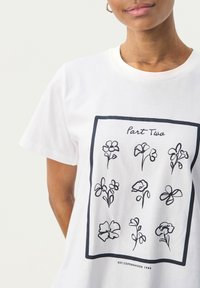 T-shirt bianco in cotone con una linea nera che disegna fiori in un motivo a griglia, con il testo "Part Two" sopra e "EST. COPENHAGEN 1986" sotto.