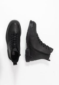 Botas de cuero negro con un diseño de caña alta, cierre con cordones en el frente y cremallera lateral. Cuenta con una suela de goma texturizada y punta redonda.