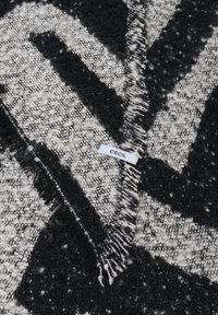 Svart och vit mönstrad scarf med en strukturerad väv, med fransiga kanter och en liten etikett som säger "CECIL."