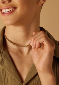 Gouden ketting choker-halsketting die rond de nek gedragen wordt, met een ontwerp van onderling verbonden schakels. Huidskleurige achtergrond met een textuur van een olijfgroene shirt.