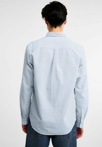 Lichtblauwe gestreepte overhemd met lange mouwen, een button-down kraag, achterste yoke detail en enkele knopenmanchetten, gecombineerd met blauwe jeans.
