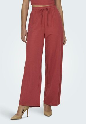 Pantaloni a gamba larga in misto cotone color ruggine con cintura elastica e dettaglio con fiocco. Abbinati a scarpe con tacco beige.
