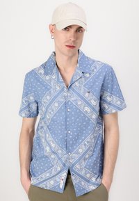 Camicia azzurra a maniche corte con motivi paisley bianchi, colletto button-down e una piccola etichetta con logo vicino all'orlo, realizzata in tessuto di cotone.