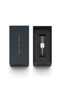 Ezüst téglalap alakú óra hálós szíjjal és fehér számlappal, sötétkék dobozban, fekete belső térrel. Arany "DANIEL WELLINGTON" felirat a dobozon.