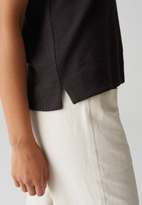 Top nero a maglia con finitura testurizzata, caratterizzato da uno spacco laterale e una vestibilità comoda, abbinato a pantaloni in lino color crema.