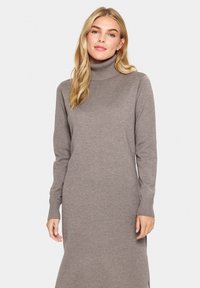 Abito a collo alto color taupe in morbido materiale knit. Presenta maniche lunghe, una vestibilità rilassata e spacchi laterali per facilitare i movimenti. Texture liscia.