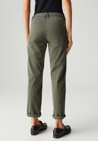 Pantaloni chino verde oliva con una vestibilità rilassata, orli arrotolati e due tasche posteriori. Realizzati in un tessuto liscio e leggero.