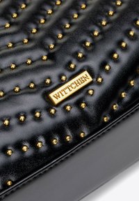 Černá kožená kabelka s pozlacenými cvočky, texturovaným povrchem a zlatou destičkou s logem "Wittchen." Strukturovaný obdélníkový design.