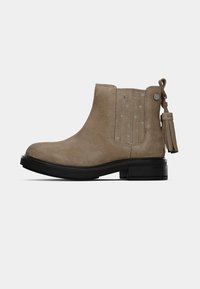 Bottines en daim beige mi-hauteur avec une semelle noire, panneau latéral élastique avec des étoiles, et une languette à franges à l'arrière.