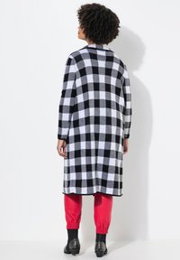 Zwart-wit geblokte lange jas met kraag, gecombineerd met rode elastische broek met manchet en gestudde zwarte laarzen. Soepele textuur.