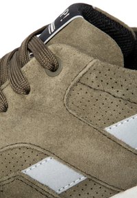 Zapato de ante marrón con detalles perforados, acentos en blanco, cordones redondos y un forro de malla negra. Diseño de puntera redondeada y marca sutil.