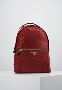 Punainen reppu, jossa on leopardikuosi, valmistettu sileästä materiaalista. Sisältää edessä vetoketjullisen taskun ja ylhäällä kahvan, brändätty "Michael Kors".