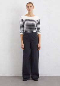 Striped long-sleeve top in cream and navy, paired with high-waisted wide-leg trousers in dark gray. Smooth fabric, relaxed fit.