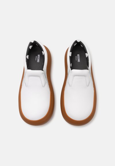 White slip-on shoes with a smooth leather upper, brown rubber outsole, and a black interior featuring a white polka dot pattern.