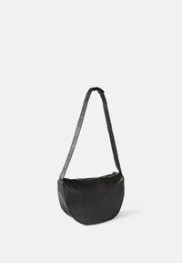 Black leather shoulder bag with a curved silhouette, covered zipper, and a flat strap featuring adjustable holes for length.