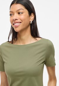 Olivgrön, figurnära t-shirt med vid halsringning och korta ärmar. Tyget verkar mjukt och slätt med minimala synliga sömmar.