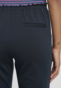 Tumedad elastsed püksid elastse vöökohtaga, ühekordse tagataskuga. Pehme tekstuur ja sile viimistlus.