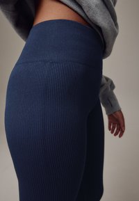 Mørkeblå ribstrikkede leggings med høj talje, med en glat tekstur og tætsiddende design, kombineret med en lysegrå sweatshirt.