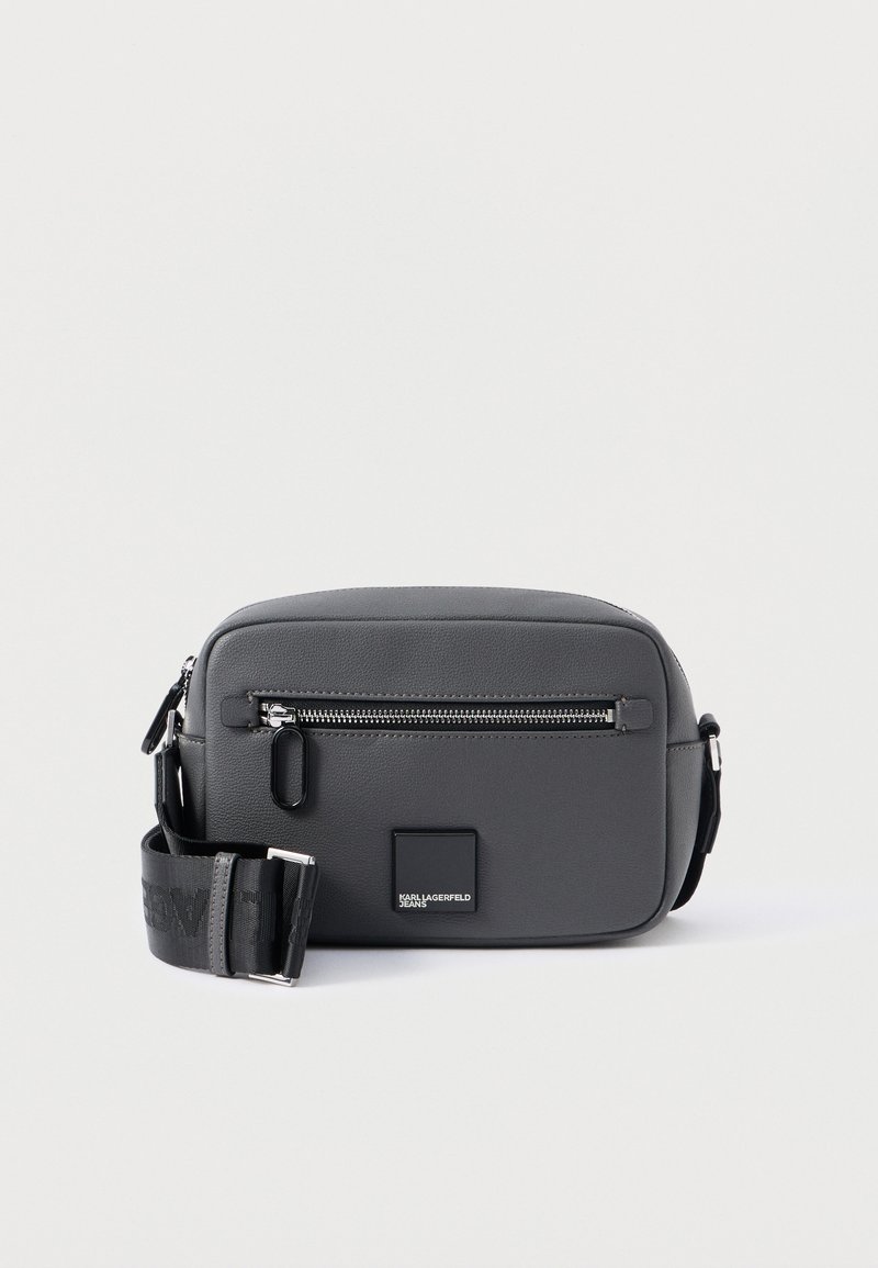 Bolsa transversal compacta em cinza escuro com bolso frontal com fecho, alça preta ajustável e pequeno logótipo quadrado.