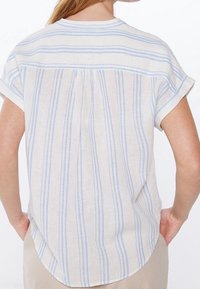 Chemise en lin léger à manches courtes avec rayures bleues et blanches, présentant une coupe décontractée et un pli au niveau de l'encolure arrière.