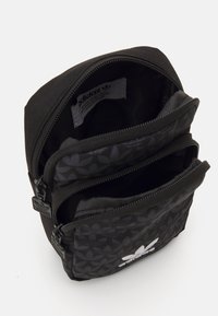 Bolsita de tela negra con tres compartimentos con cremallera, que presenta un patrón floral, superficie texturizada y un logo bordado en la parte delantera.