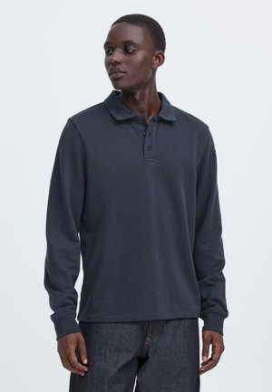 Dunkelblaue Langarm-Poloshirt mit Kragen und Dreiknopf-Leiste, aus weichem Stoff, kombiniert mit dunklen Jeans.