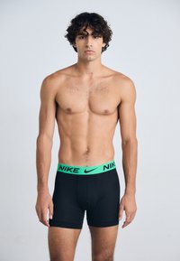 Boxers noirs Nike avec une ceinture néon verte portant le logo Nike, fabriqués en tissu extensible, conçus pour le confort et l'ajustement.
