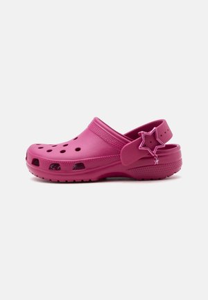 Zoccolo magenta slip-on con fori di ventilazione, suola testurizzata, cinturino regolabile al tallone e ciondolo a forma di stella sul cinturino.