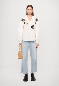 Weiße Bluse mit Stickerei, Puffärmel und Kragen. Helle blaue Jeans mit ausgefranstem Saum. Schwarze Stiefel und eine geflochtene Handtasche.