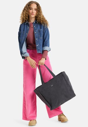 Sac fourre-tout noir avec deux poignées, fabriqué à partir d'un matériau durable. Présente un logo discret sur le devant, associé à une veste en denim et un pantalon en velours côtelé rose.