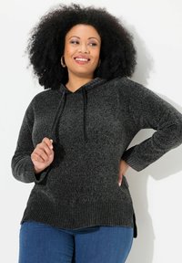 Hoodie in donkergrijze textuurgebreide stof met geribbelde manchetten en onderkant; voorzien van zijsplitten voor meer bewegingsgemak. Gepaarde met blauwe jeans.
