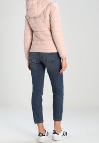 Giacca a vento leggera rosa con cappuccio, polsini a costine e texture liscia, abbinata a jeans blu scuro e sneakers bianche e nere.