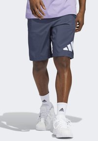 Marinblå idrottsshorts med vitt Adidas-logotyp, gjorda av lätt material med en slät yta, knälånga, och med sidoklyftor.