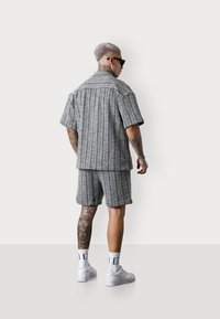 Grau gestreiftes Kurzarmhemd und passende Shorts aus leichtem Material. Weiße Turnschuhe und gemusterte Tattoos sind sichtbar.
