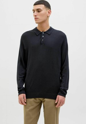 Camisa polo negra de manga larga con color, tapeta de tres botones y puños de canalé; combinada con pantalones caqui; textura suave.