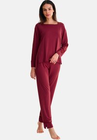 Ensemble de détente bordeaux comprenant un haut à manches longues avec fentes sur les côtés et un pantalon avec des accents en dentelle au niveau de l'ourlet. Tissu doux, coupe décontractée.