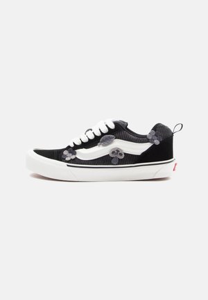 Sorte corduroy sneakers med hvide læderdetaljer, prydet med blomsterapplikationer i nuancer af grå og en hvid gummisål. Klassisk snørebåndsdesign.